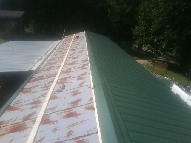 Old rusted panels beside newly installed green metal roofing — Wind Damage Roof Repair by Roofing Brothers in Forks