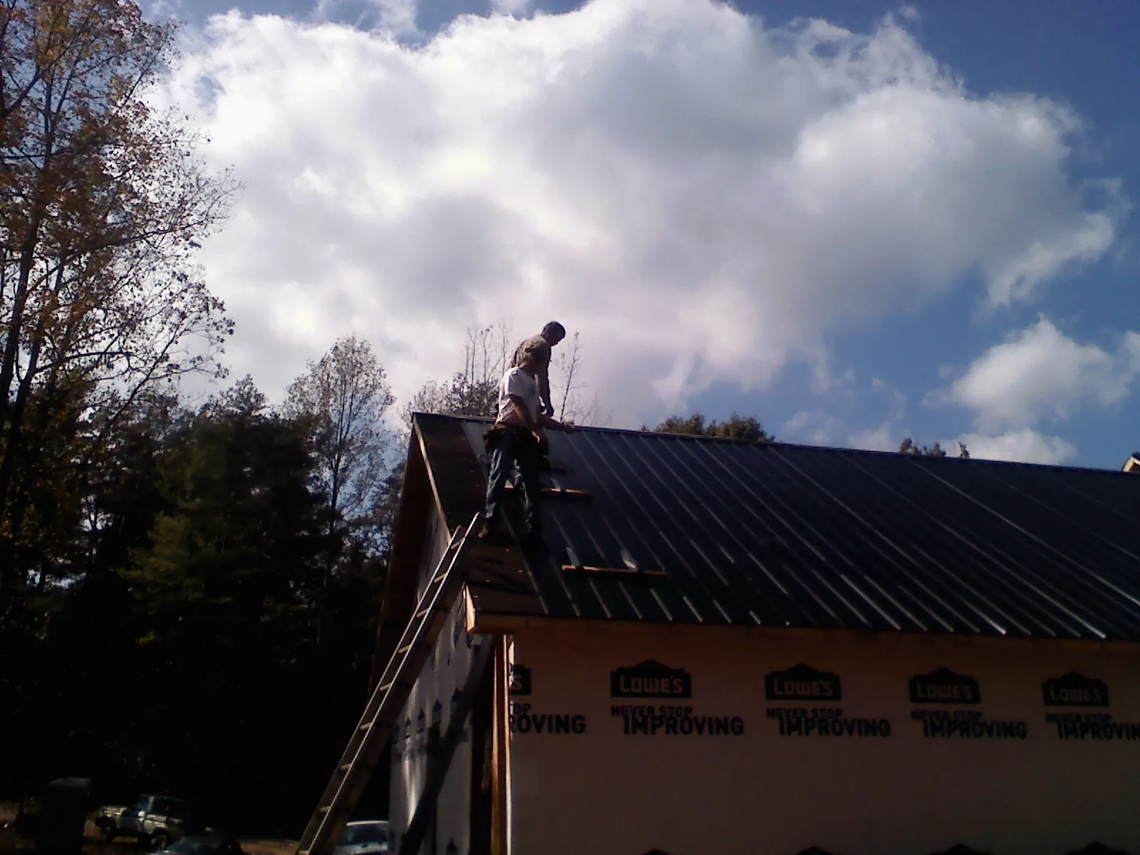 Roofer fastening dark metal panels high against a cloudy sky in Forks