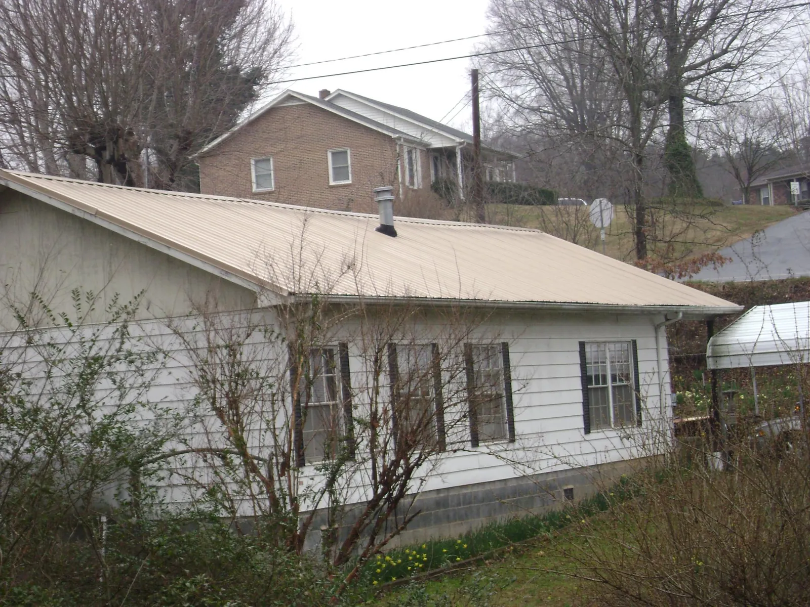 Tan metal roof on a white sided house set into a hillside — Commercial Roofing by Roofing Brothers in Forks